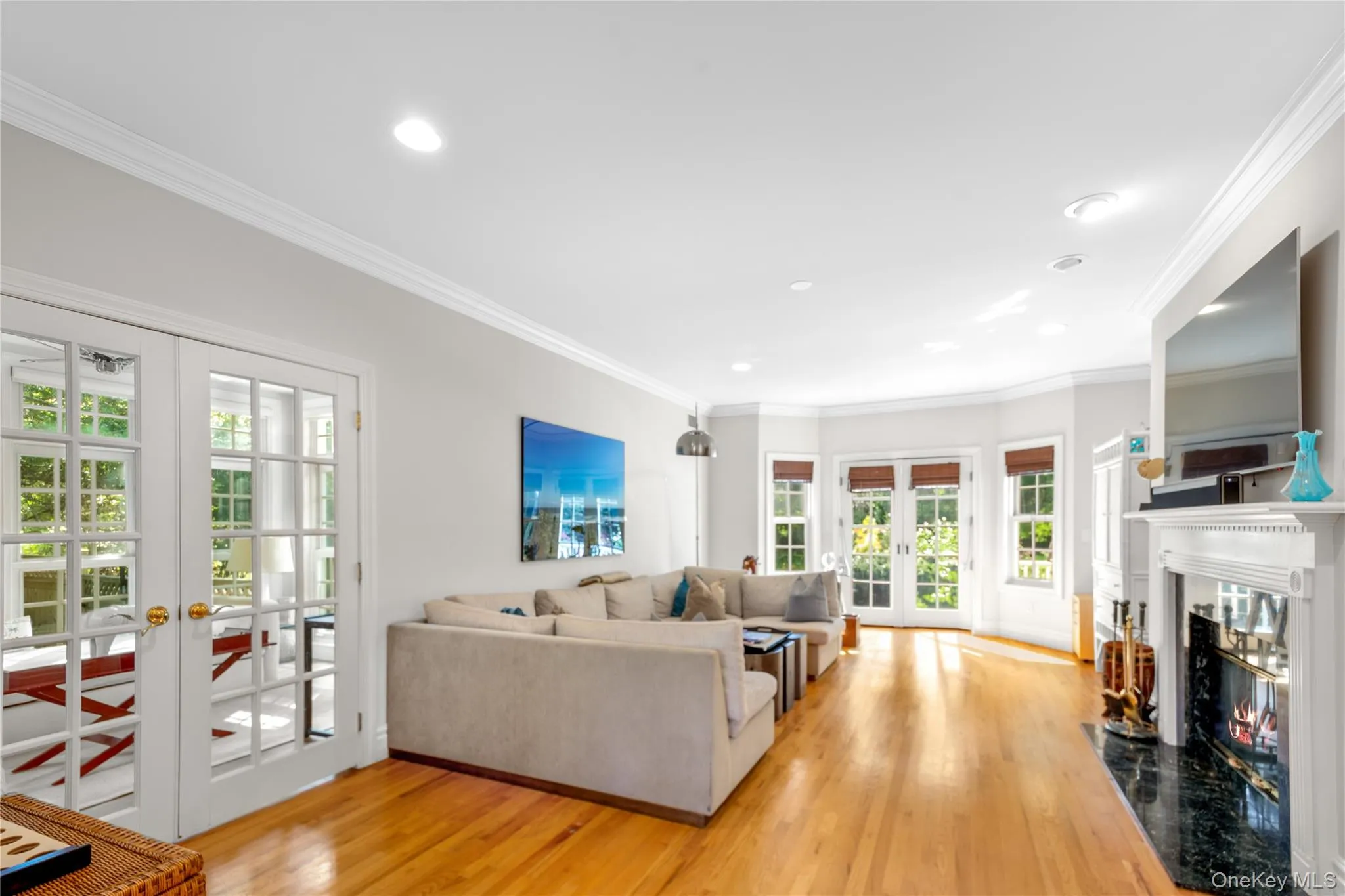 Living area featuring french doors, crown molding, light wood-style floors, a premium fireplace, and recessed lighting Living area featuring french doors, crown molding, light wood-style floors, a premium fireplace, and recessed lighting