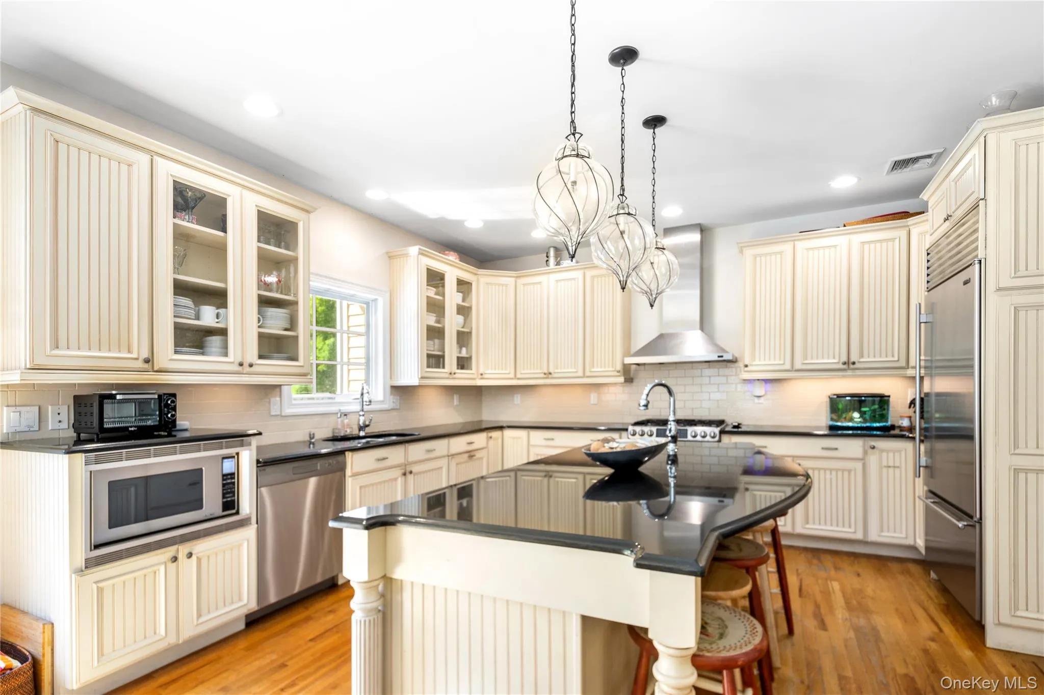 Kitchen featuring cream cabinetry, glass insert cabinets, an island with sink, light wood-style flooring, and a kitchen bar Kitchen featuring cream cabinetry, glass insert cabinets, an island with sink, light wood-style flooring, and a kitchen bar