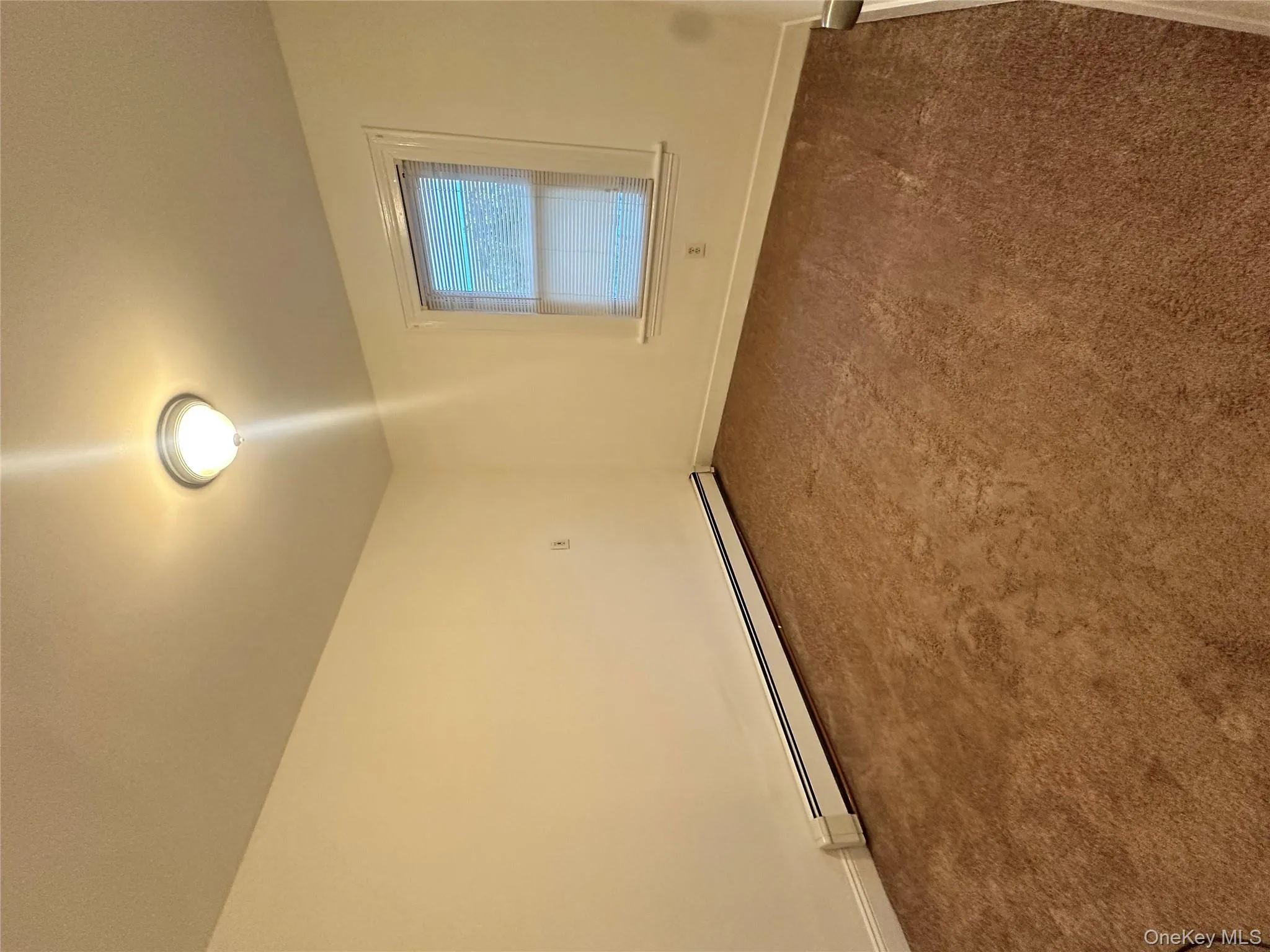 Empty room featuring dark carpet and a baseboard heating unit Empty room featuring dark carpet and a baseboard heating unit