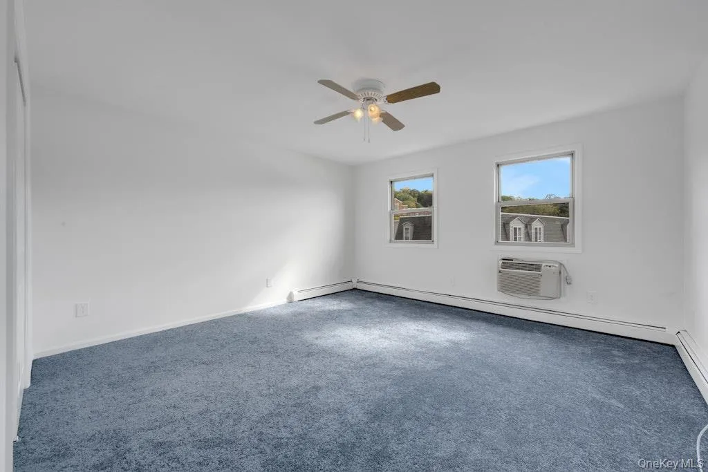 Spare room with an AC wall unit, carpet, a ceiling fan, and baseboard heating Spare room with an AC wall unit, carpet, a ceiling fan, and baseboard heating