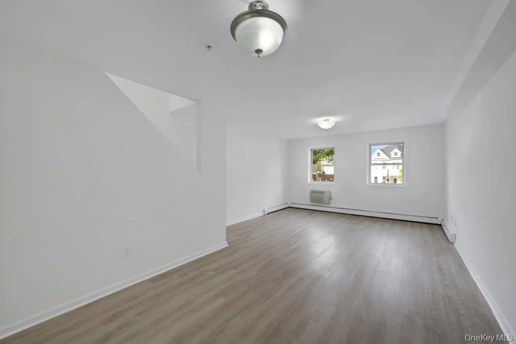 Empty room with an AC wall unit, light wood-style floors, and a baseboard heating unit Empty room with an AC wall unit, light wood-style floors, and a baseboard heating unit