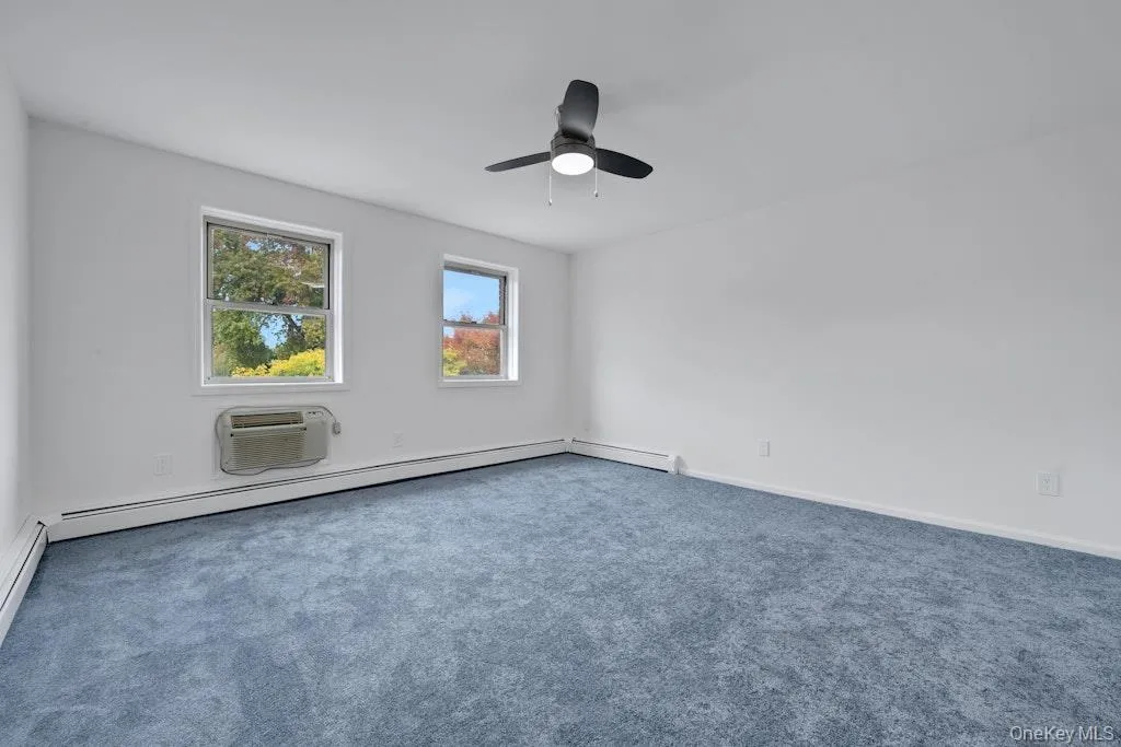 Carpeted spare room featuring an AC wall unit, a ceiling fan, and a baseboard heating unit Carpeted spare room featuring an AC wall unit, a ceiling fan, and a baseboard heating unit