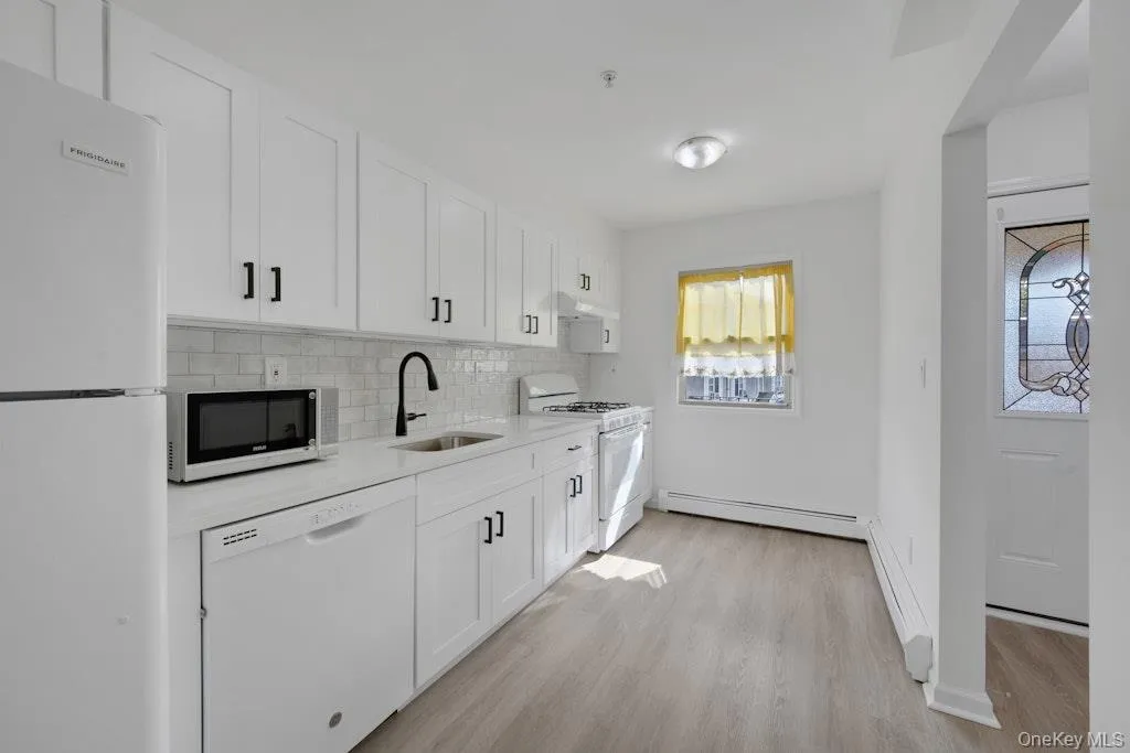Kitchen with white appliances, white cabinets, decorative backsplash, and light wood-style floors Kitchen with white appliances, white cabinets, decorative backsplash, and light wood-style floors