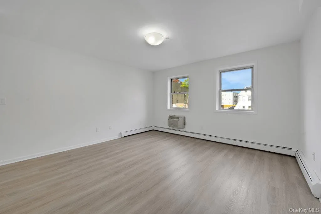 Spare room featuring light wood finished floors, a wall mounted AC, and baseboard heating Spare room featuring light wood finished floors, a wall mounted AC, and baseboard heating