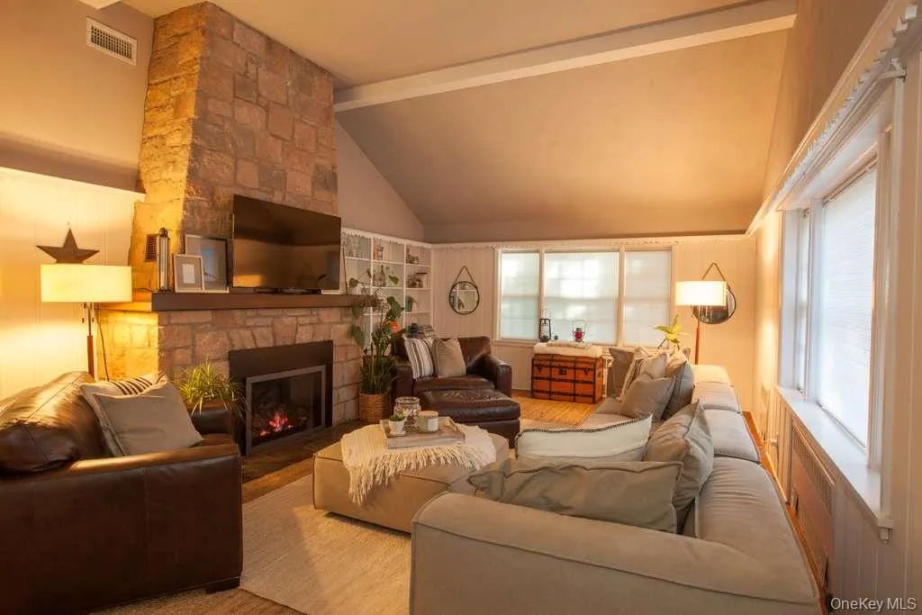 Living room featuring healthy amount of natural light, a stone fireplace, and wood finished floors Living room featuring healthy amount of natural light, a stone fireplace, and wood finished floors