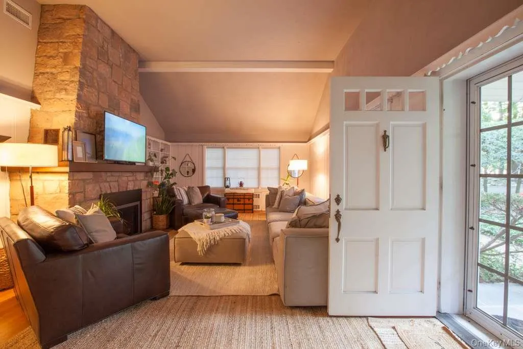Living area featuring plenty of natural light, vaulted ceiling, a stone fireplace, and wood finished floors Living area featuring plenty of natural light, vaulted ceiling, a stone fireplace, and wood finished floors
