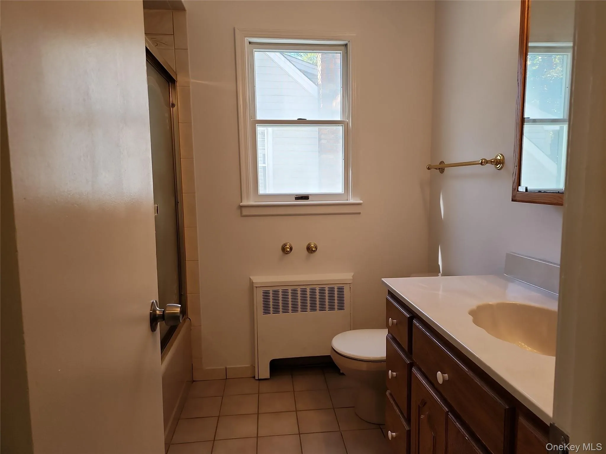 Full bath with radiator, light tile patterned floors, vanity, and shower / bath combination with glass door Full bath with radiator, light tile patterned floors, vanity, and shower / bath combination with glass door