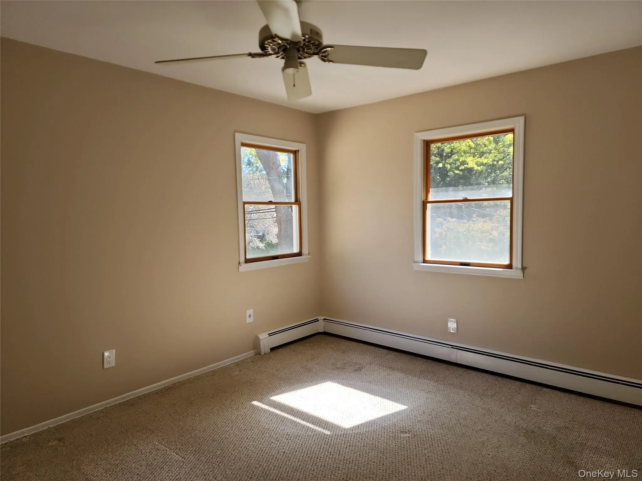 Carpeted empty room with a baseboard radiator and ceiling fan Carpeted empty room with a baseboard radiator and ceiling fan
