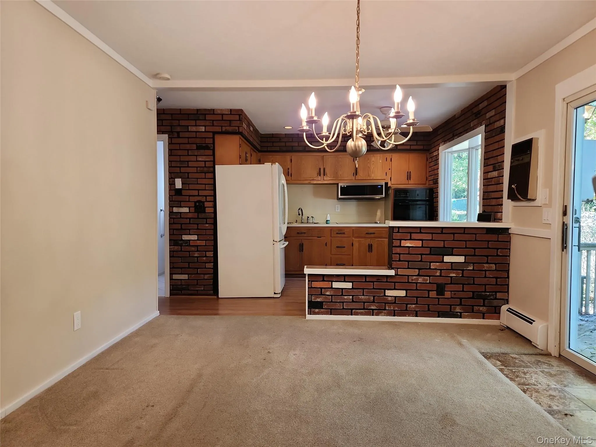 Kitchen with brick wall, freestanding refrigerator, light carpet, baseboard heating, and black oven Kitchen with brick wall, freestanding refrigerator, light carpet, baseboard heating, and black oven