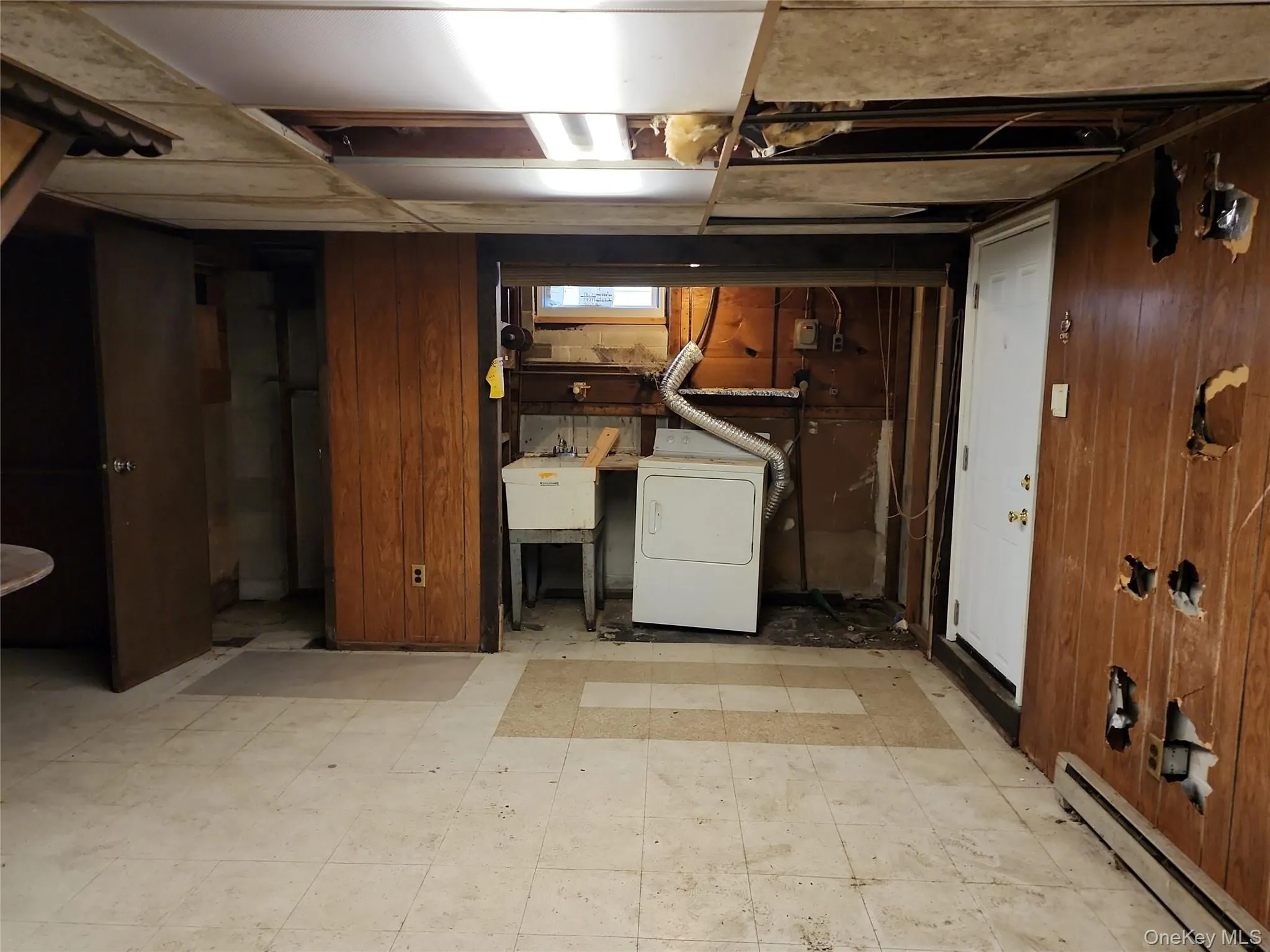 Below grade area with a baseboard heating unit, light flooring, wood walls, and washer / clothes dryer Below grade area with a baseboard heating unit, light flooring, wood walls, and washer / clothes dryer