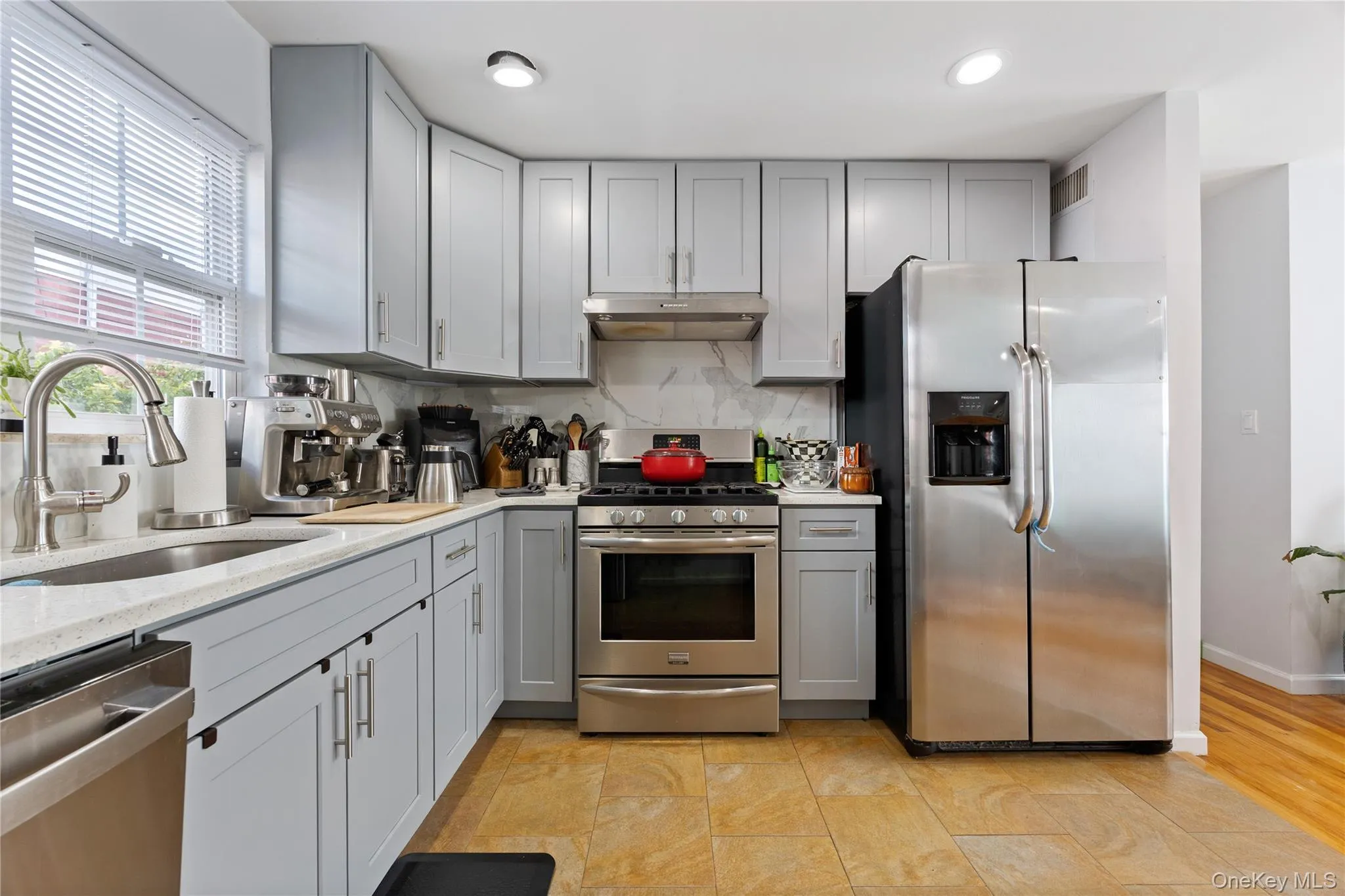 Kitchen featuring appliances with stainless steel finishes, gray cabinets, light stone countertops, tasteful backsplash, and under cabinet range hood Kitchen featuring appliances with stainless steel finishes, gray cabinets, light stone countertops, tasteful backsplash, and under cabinet range hood
