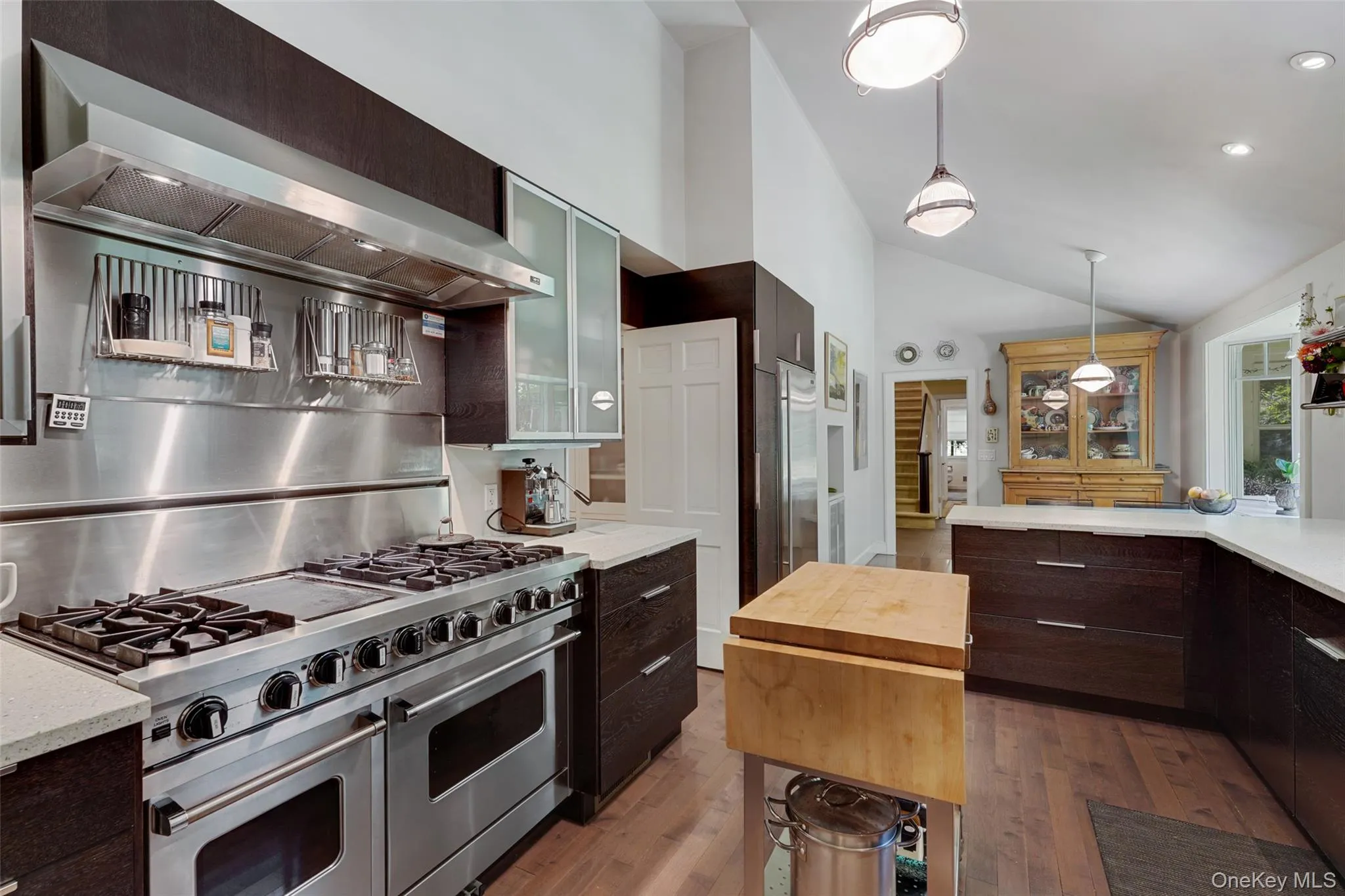 Kitchen with hanging light fixtures, dark brown cabinetry, glass insert cabinets, light wood-style floors, and premium appliances Kitchen with hanging light fixtures, dark brown cabinetry, glass insert cabinets, light wood-style floors, and premium appliances