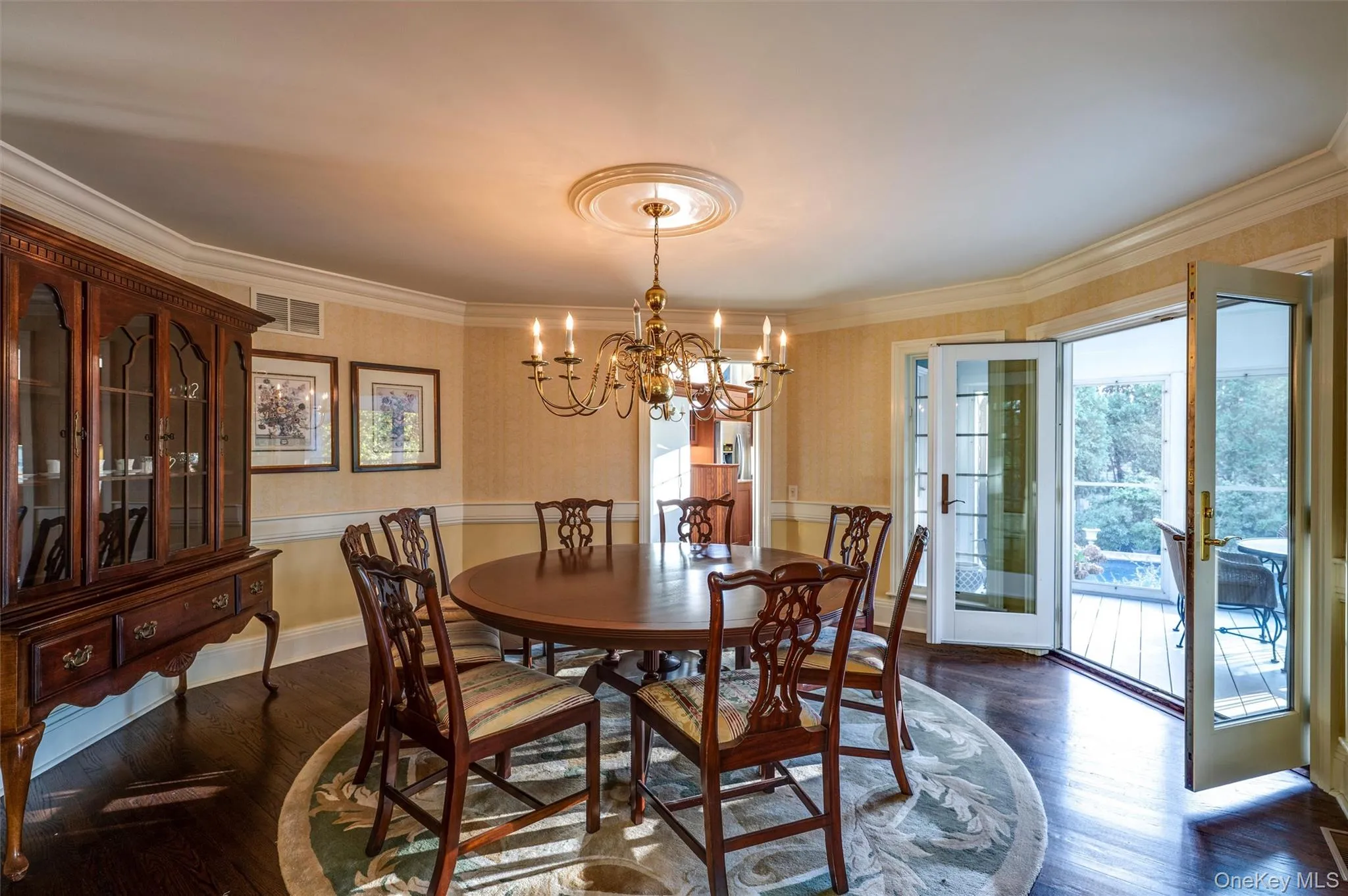 Dining space featuring dark wood-style flooring, wallpapered walls, a chandelier, and ornamental molding Dining space featuring dark wood-style flooring, wallpapered walls, a chandelier, and ornamental molding