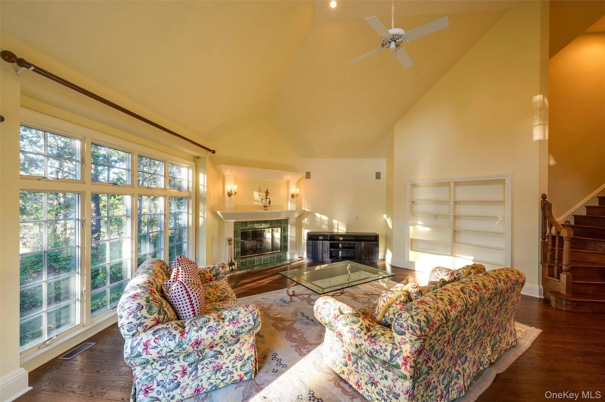 Living area with a tile fireplace, high vaulted ceiling, stairs, dark wood-type flooring, and ceiling fan Living area with a tile fireplace, high vaulted ceiling, stairs, dark wood-type flooring, and ceiling fan