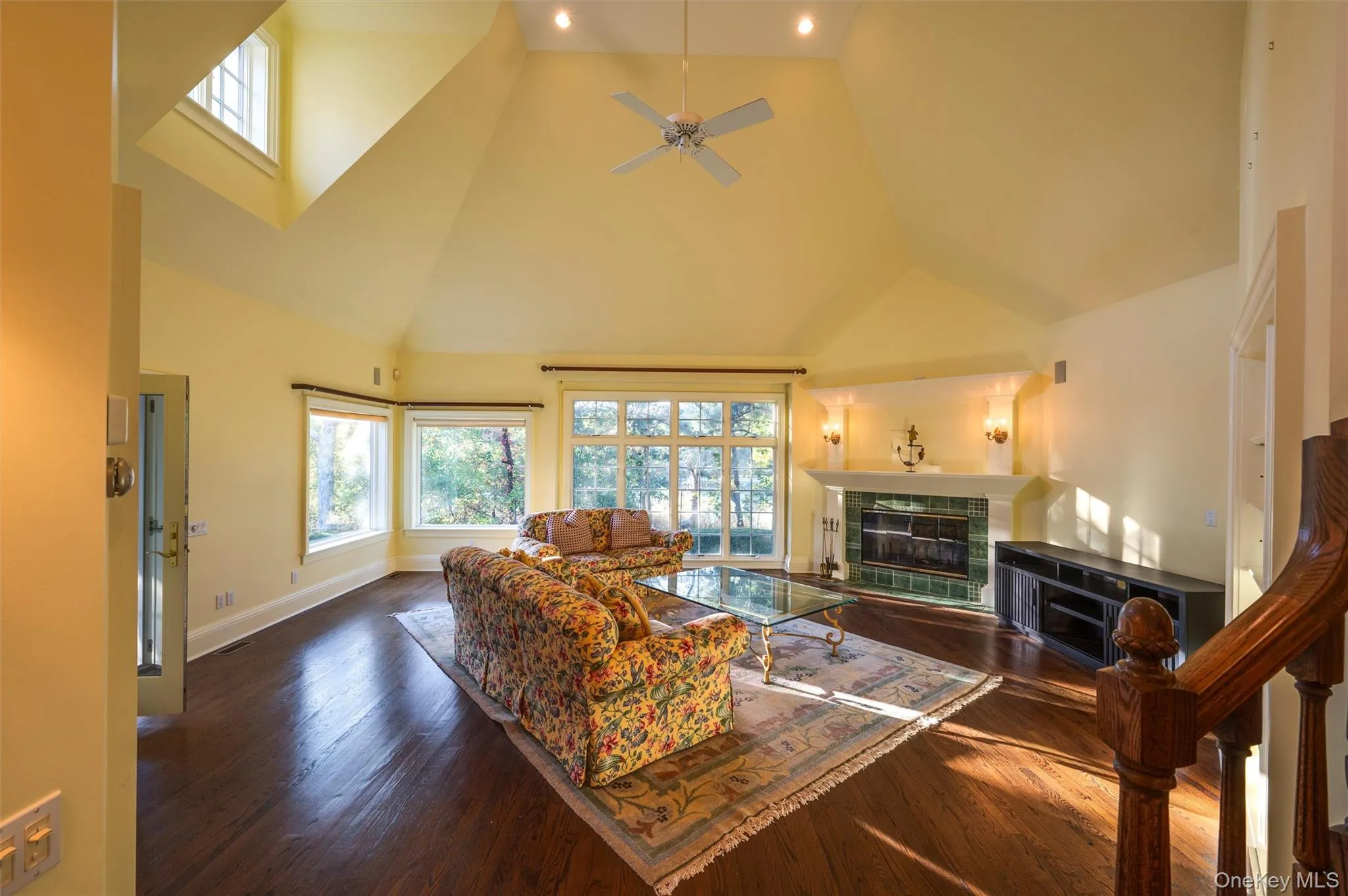 Living area featuring high vaulted ceiling, plenty of natural light, dark wood-style flooring, a tile fireplace, and a ceiling fan Living area featuring high vaulted ceiling, plenty of natural light, dark wood-style flooring, a tile fireplace, and a ceiling fan