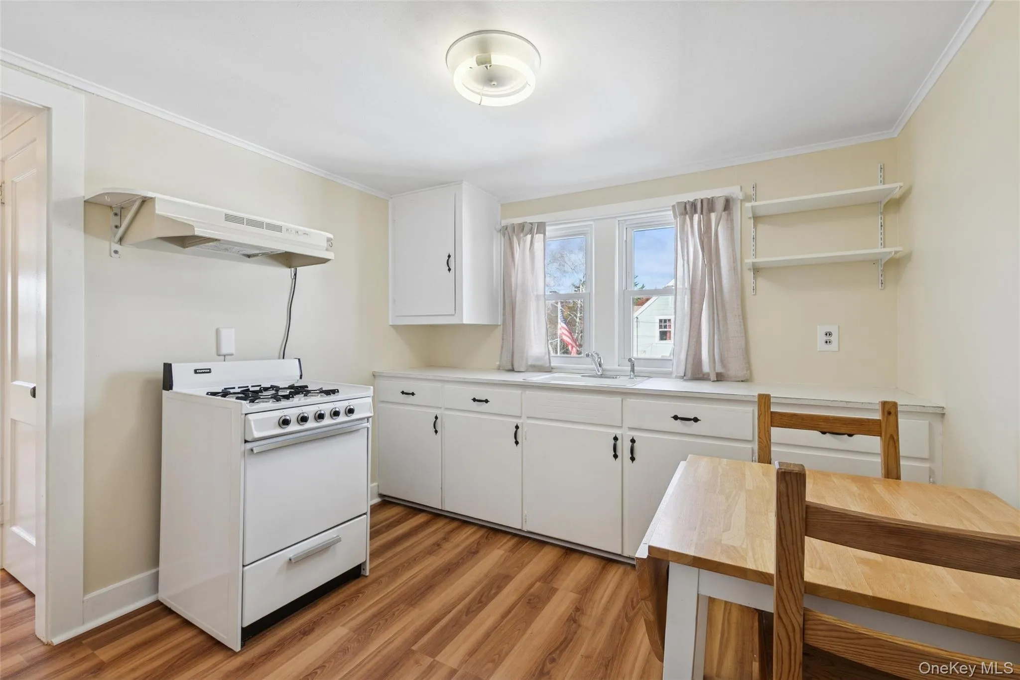 Kitchen with white gas range oven, white cabinetry, light countertops, light wood-style floors, and under cabinet range hood Kitchen with white gas range oven, white cabinetry, light countertops, light wood-style floors, and under cabinet range hood
