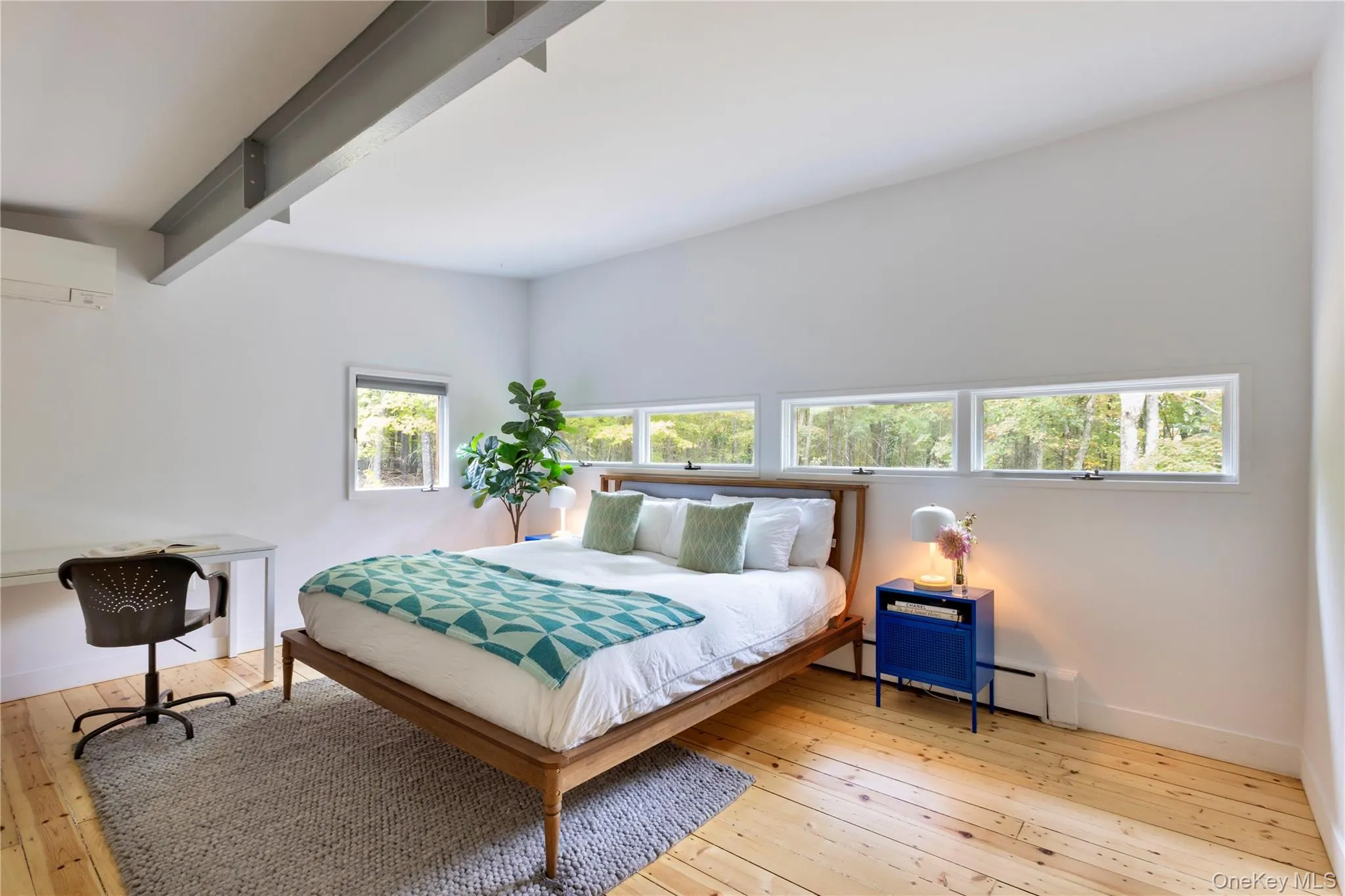 Bedroom featuring light wood-type flooring, an AC wall unit, a baseboard heating unit, beam ceiling, and a desk Bedroom featuring light wood-type flooring, an AC wall unit, a baseboard heating unit, beam ceiling, and a desk