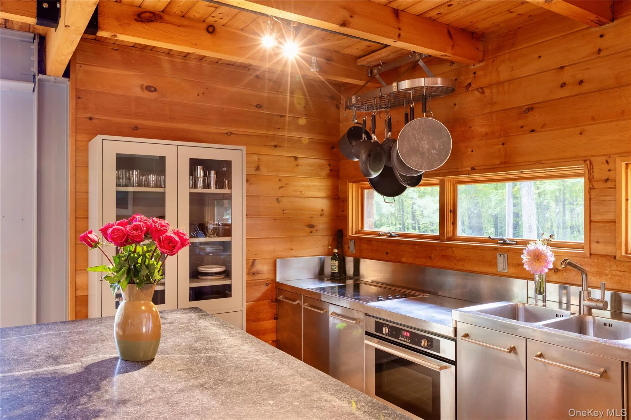 Kitchen with stainless steel counters, oven, wood walls, black electric stovetop, and a wooden ceiling with exposed beams Kitchen with stainless steel counters, oven, wood walls, black electric stovetop, and a wooden ceiling with exposed beams