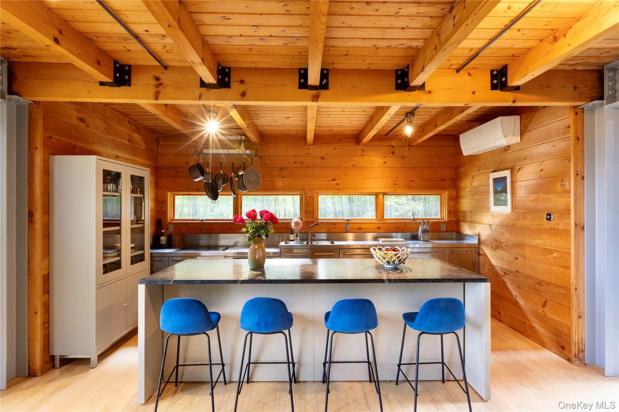 Kitchen featuring wooden walls, a breakfast bar area, light wood-style floors, a spacious island, and a wood ceiling with exposed beams Kitchen featuring wooden walls, a breakfast bar area, light wood-style floors, a spacious island, and a wood ceiling with exposed beams