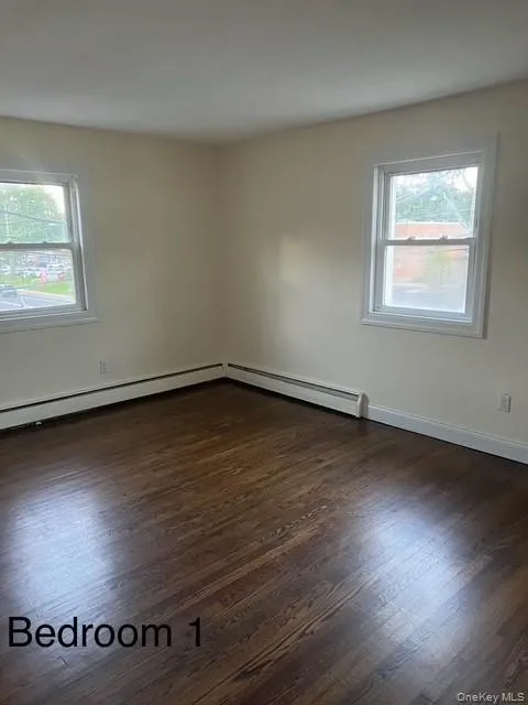 Empty room with dark wood-type flooring and baseboard heating Empty room with dark wood-type flooring and baseboard heating