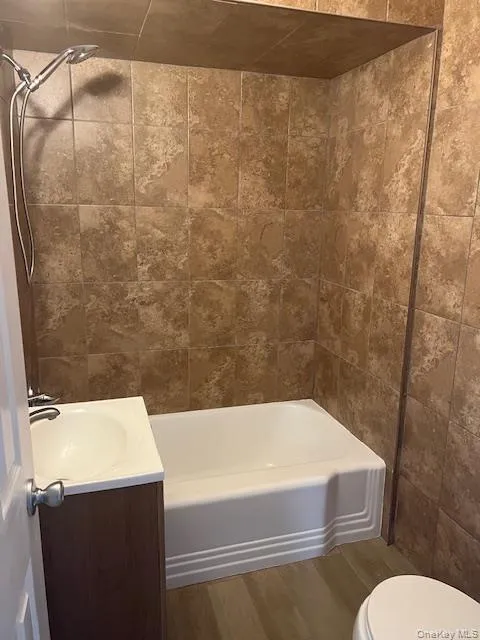 Full bathroom with vanity, bathing tub / shower combination, dark wood-type flooring, and tile walls Full bathroom with vanity, bathing tub / shower combination, dark wood-type flooring, and tile walls