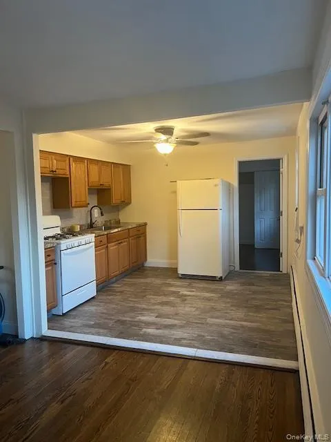Kitchen with dark wood finished floors, white appliances, a baseboard heating unit, brown cabinets, and a ceiling fan Kitchen with dark wood finished floors, white appliances, a baseboard heating unit, brown cabinets, and a ceiling fan