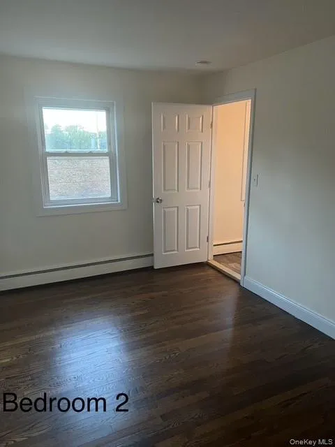 Empty room featuring a baseboard heating unit and dark wood-style flooring Empty room featuring a baseboard heating unit and dark wood-style flooring