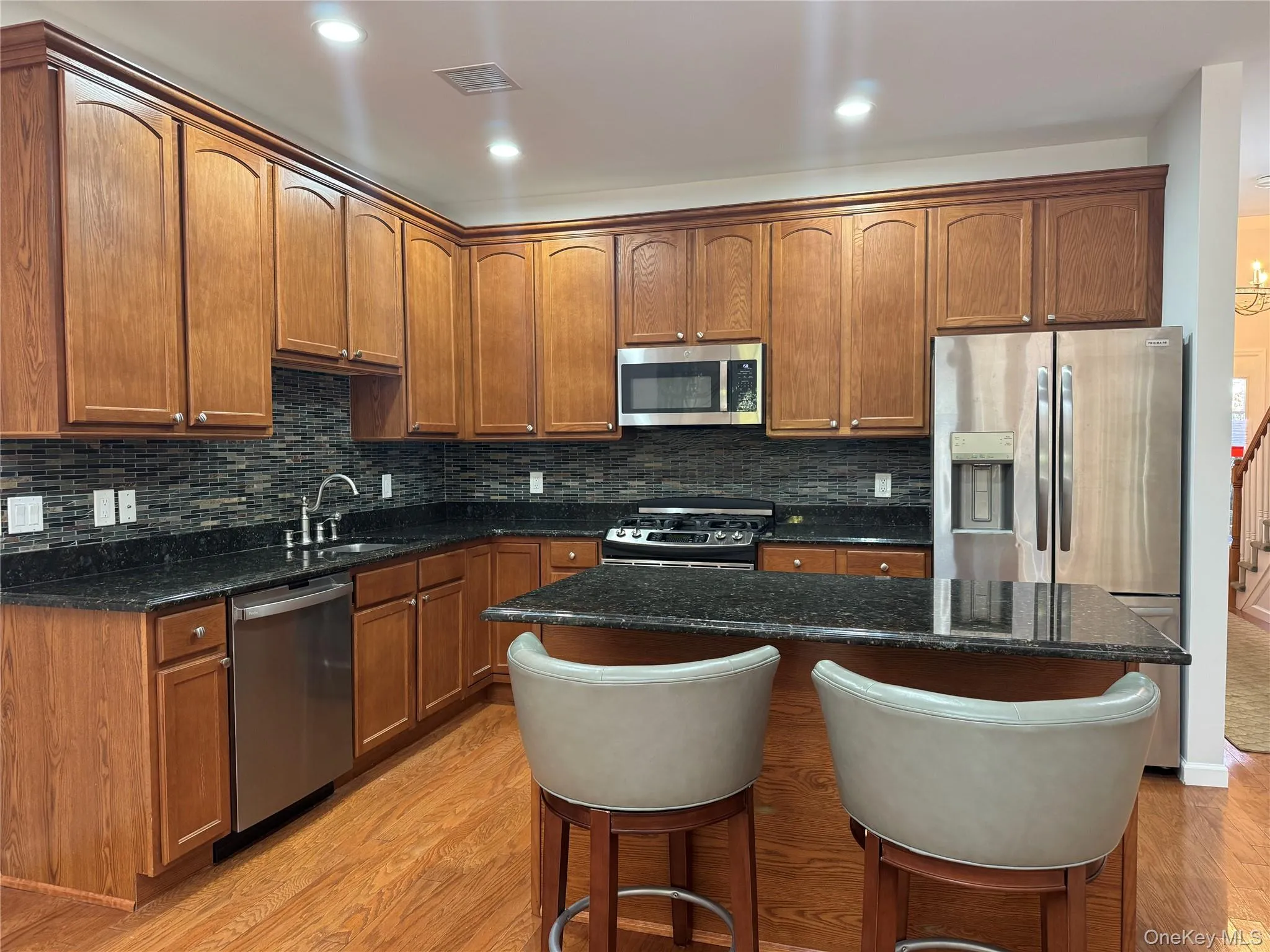Kitchen featuring a kitchen breakfast bar, decorative backsplash, appliances with stainless steel finishes, light wood finished floors, and dark stone countertops Kitchen featuring a kitchen breakfast bar, decorative backsplash, appliances with stainless steel finishes, light wood finished floors, and dark stone countertops