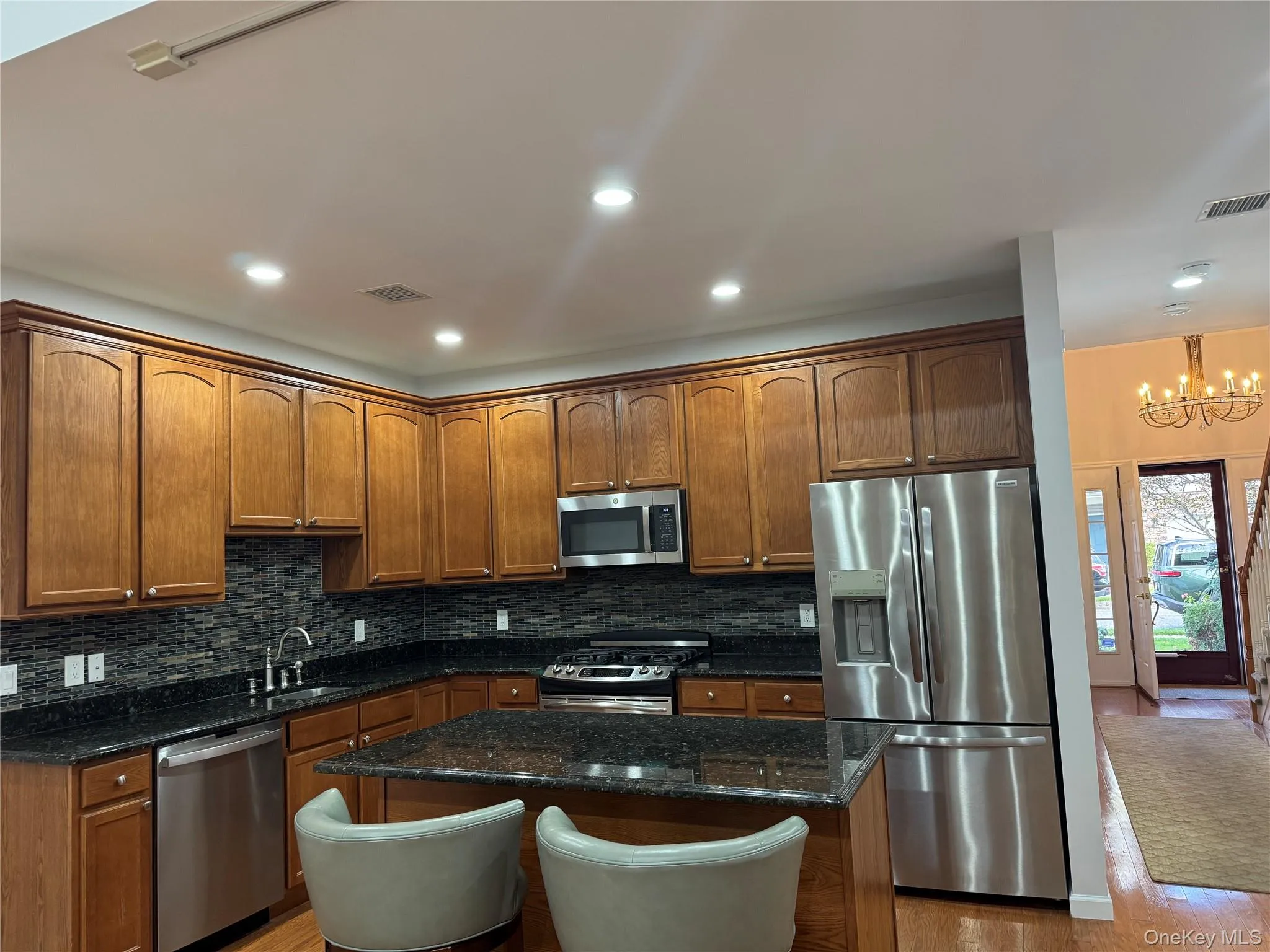 Kitchen featuring appliances with stainless steel finishes, backsplash, dark stone counters, a kitchen island, and recessed lighting Kitchen featuring appliances with stainless steel finishes, backsplash, dark stone counters, a kitchen island, and recessed lighting
