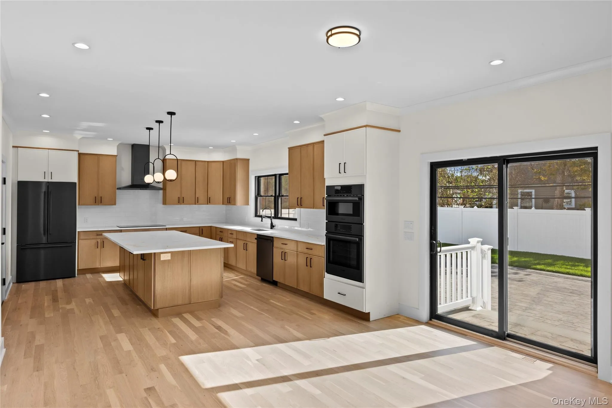 Kitchen featuring black appliances, light wood-style floors, pendant lighting, a kitchen island, and tasteful backsplash Kitchen featuring black appliances, light wood-style floors, pendant lighting, a kitchen island, and tasteful backsplash