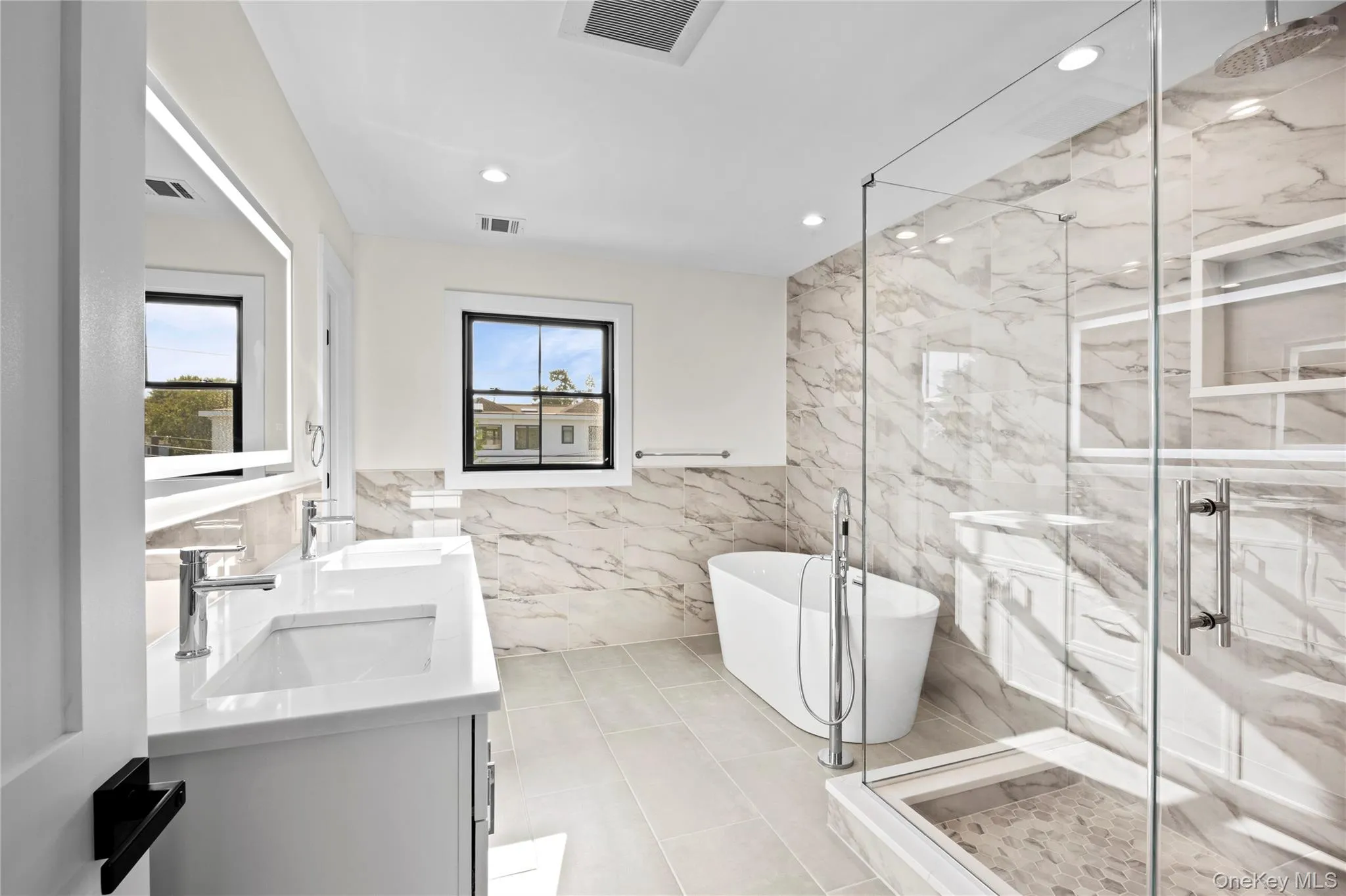 Full bath featuring tile walls, a freestanding tub, healthy amount of natural light, double vanity, and a marble finish shower Full bath featuring tile walls, a freestanding tub, healthy amount of natural light, double vanity, and a marble finish shower
