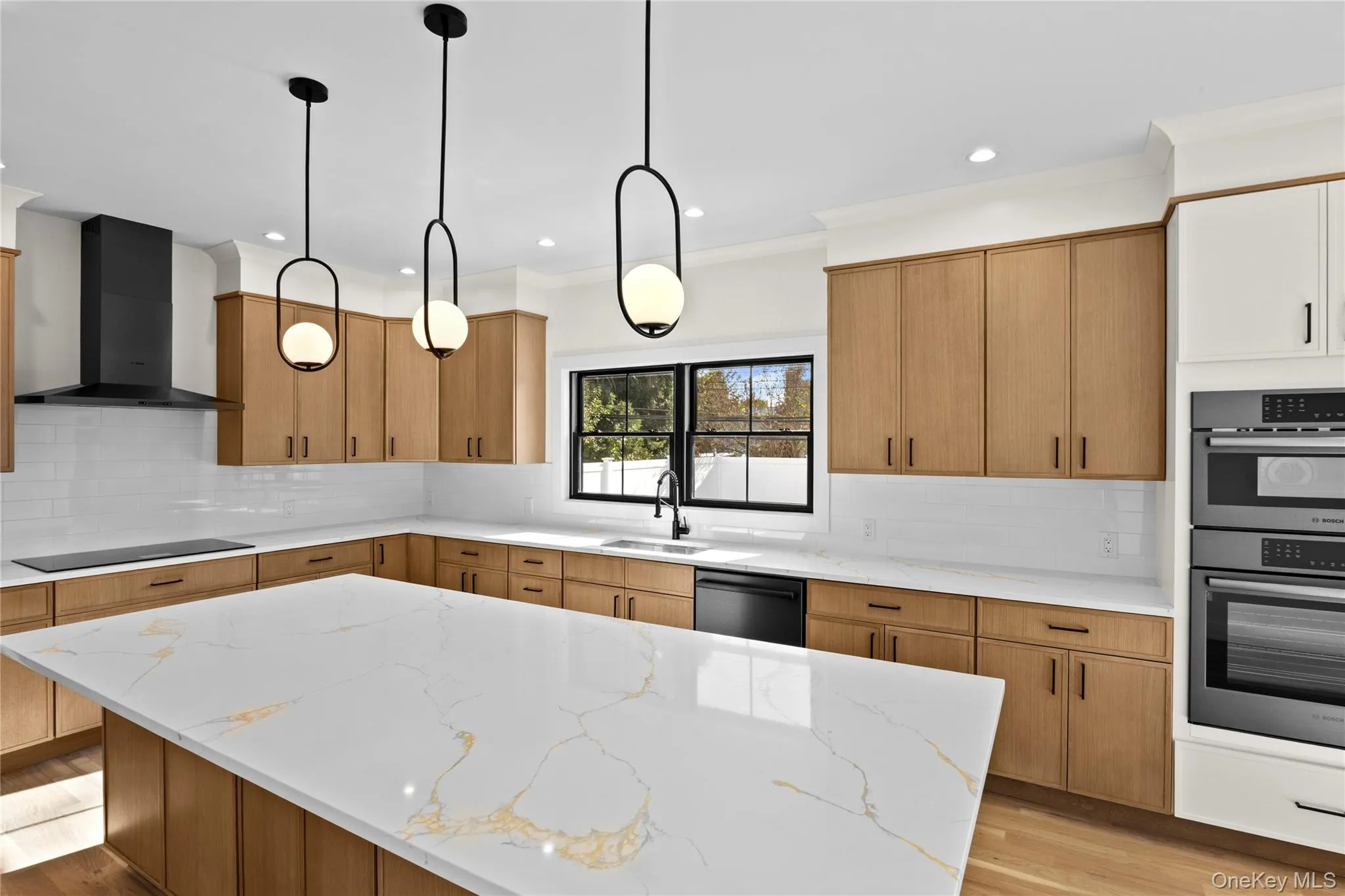 Kitchen with tasteful backsplash, light stone countertops, light wood-style flooring, wall chimney exhaust hood, and ornamental molding Kitchen with tasteful backsplash, light stone countertops, light wood-style flooring, wall chimney exhaust hood, and ornamental molding