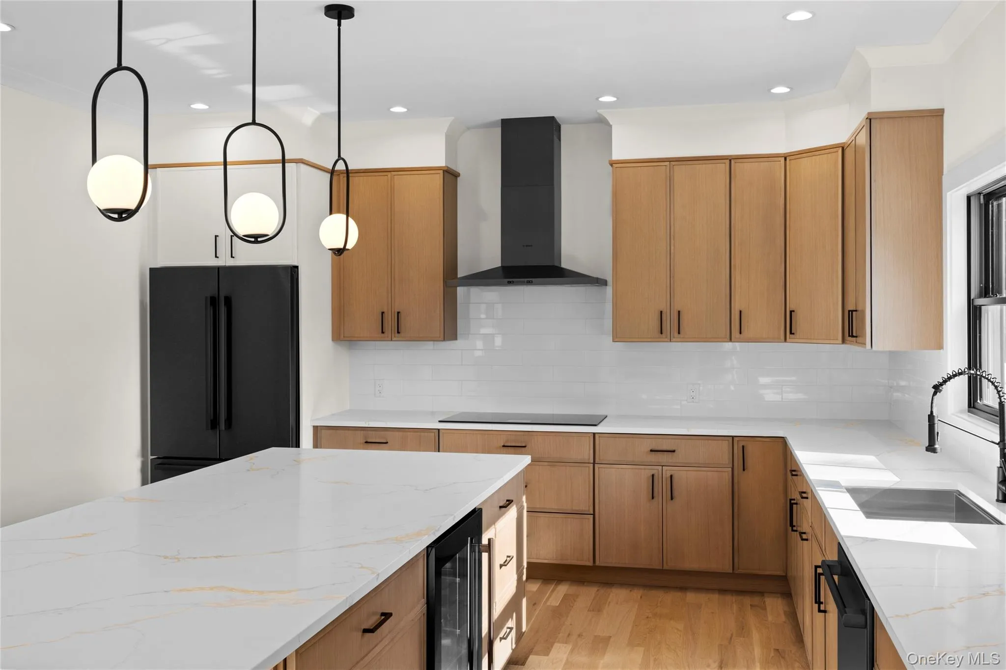 Kitchen featuring light stone counters, decorative light fixtures, wall chimney range hood, light wood-type flooring, and beverage cooler Kitchen featuring light stone counters, decorative light fixtures, wall chimney range hood, light wood-type flooring, and beverage cooler
