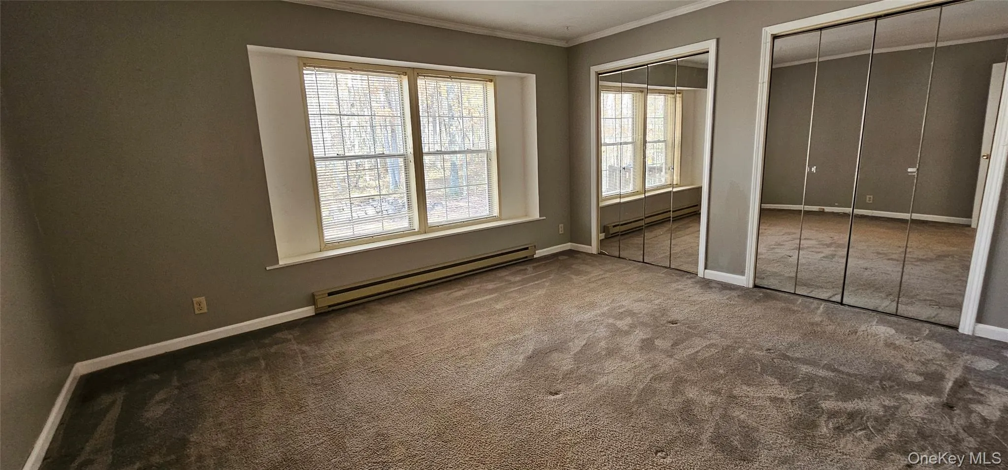 Unfurnished bedroom with multiple closets, crown molding, a baseboard radiator, and carpet Unfurnished bedroom with multiple closets, crown molding, a baseboard radiator, and carpet