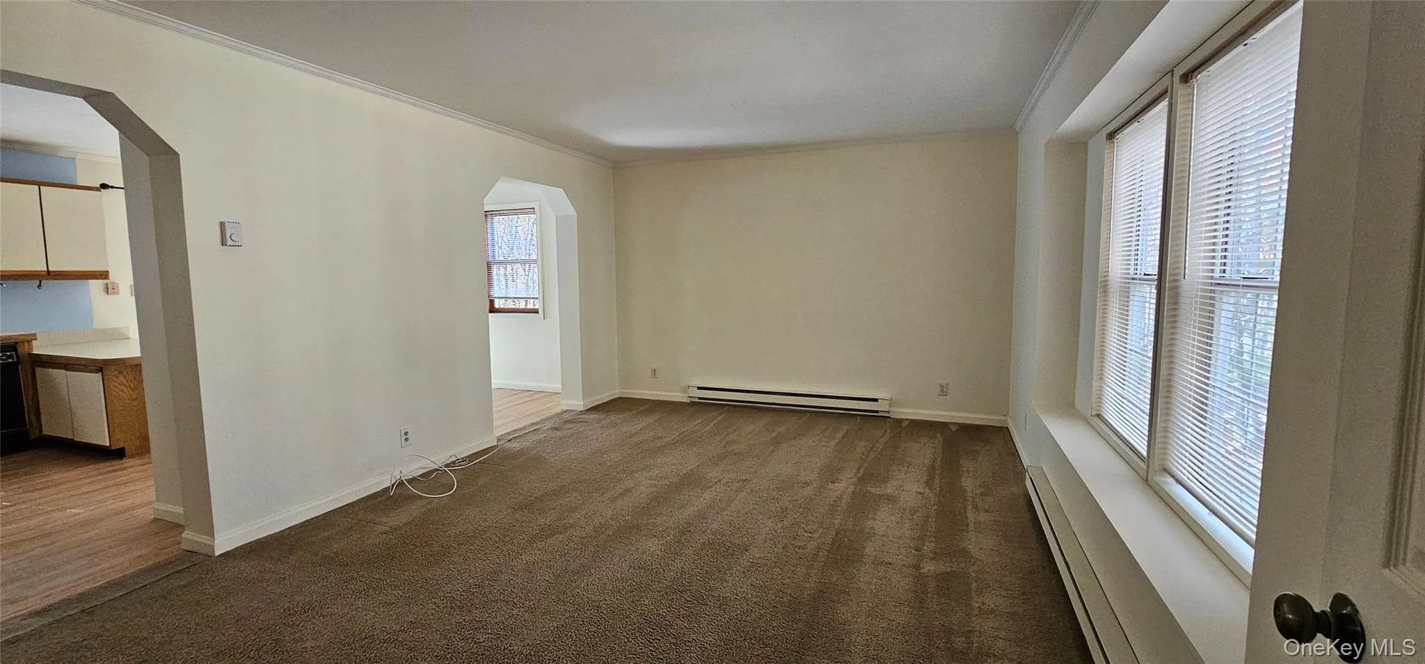 Empty room with baseboard heating, arched walkways, dark carpet, and crown molding Empty room with baseboard heating, arched walkways, dark carpet, and crown molding