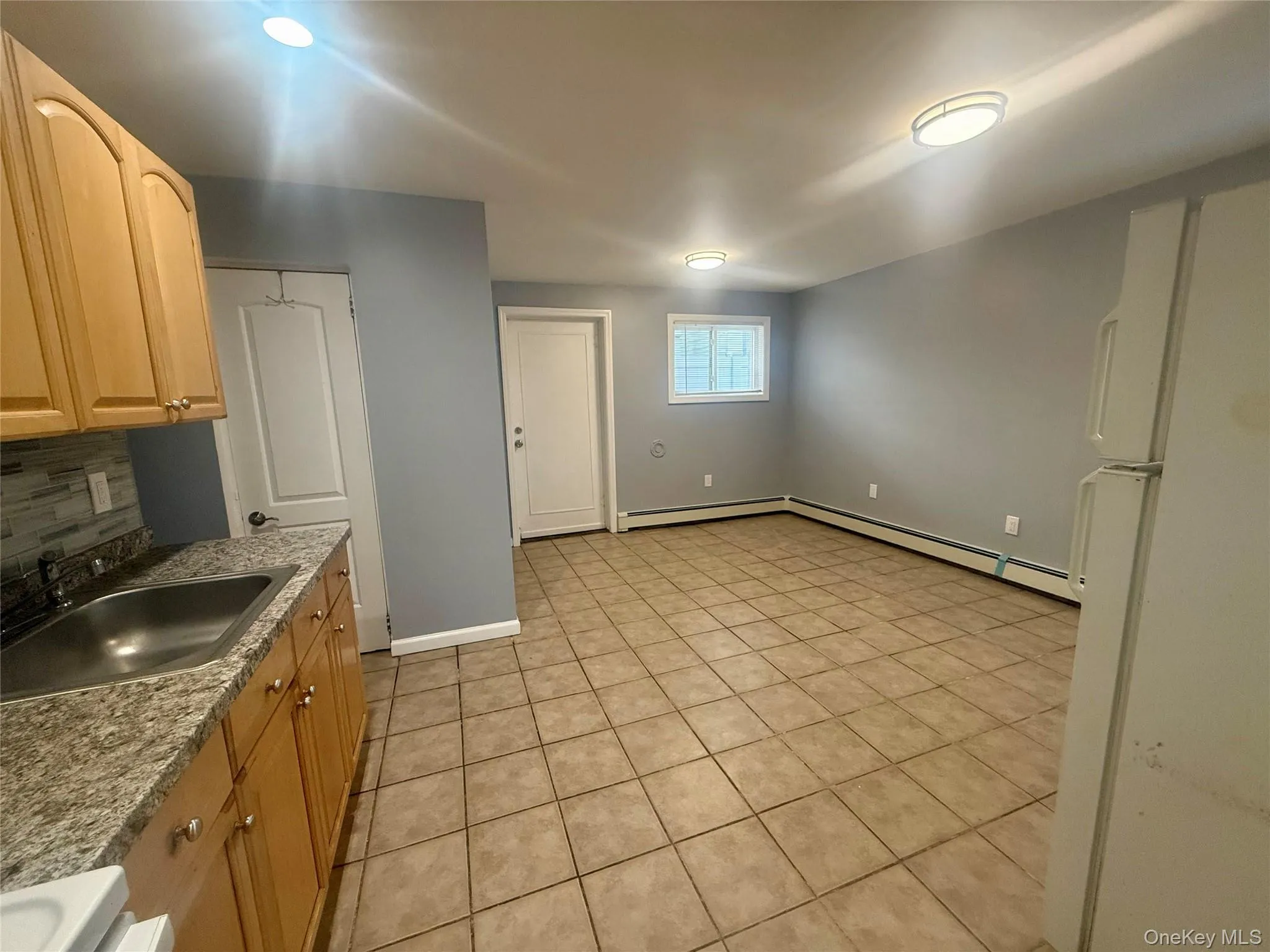 Kitchen with freestanding refrigerator, light tile patterned floors, stove, decorative backsplash, and a baseboard heating unit Kitchen with freestanding refrigerator, light tile patterned floors, stove, decorative backsplash, and a baseboard heating unit