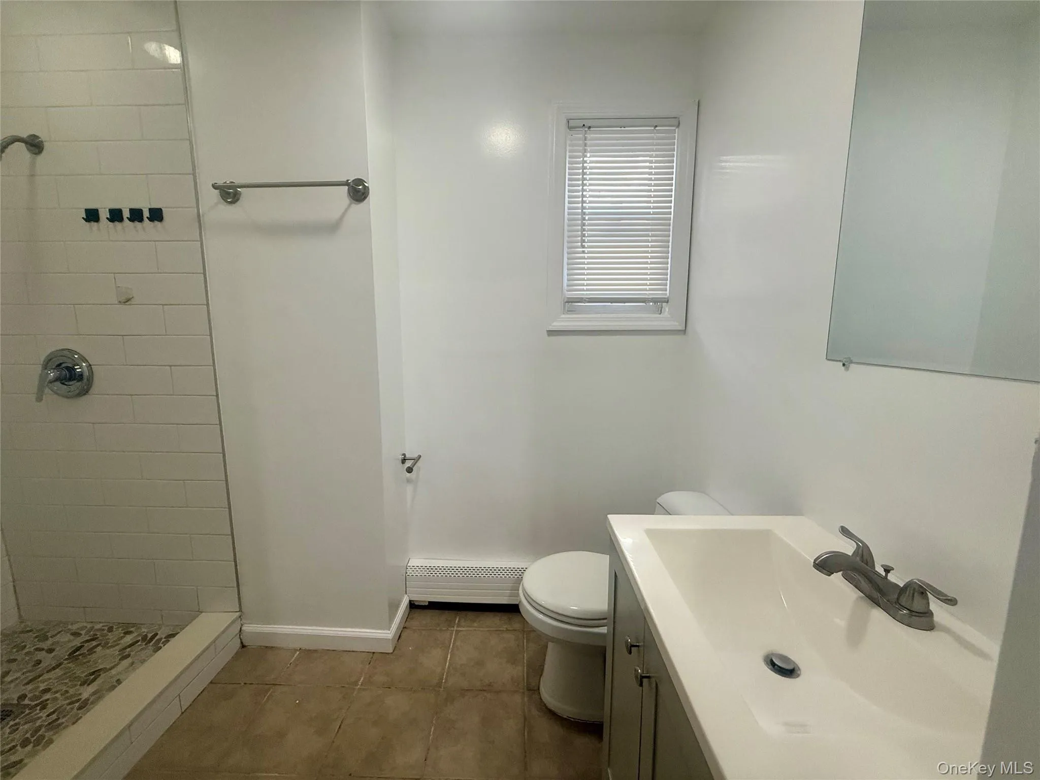Bathroom featuring vanity, a shower stall, dark tile patterned floors, and a baseboard radiator Bathroom featuring vanity, a shower stall, dark tile patterned floors, and a baseboard radiator