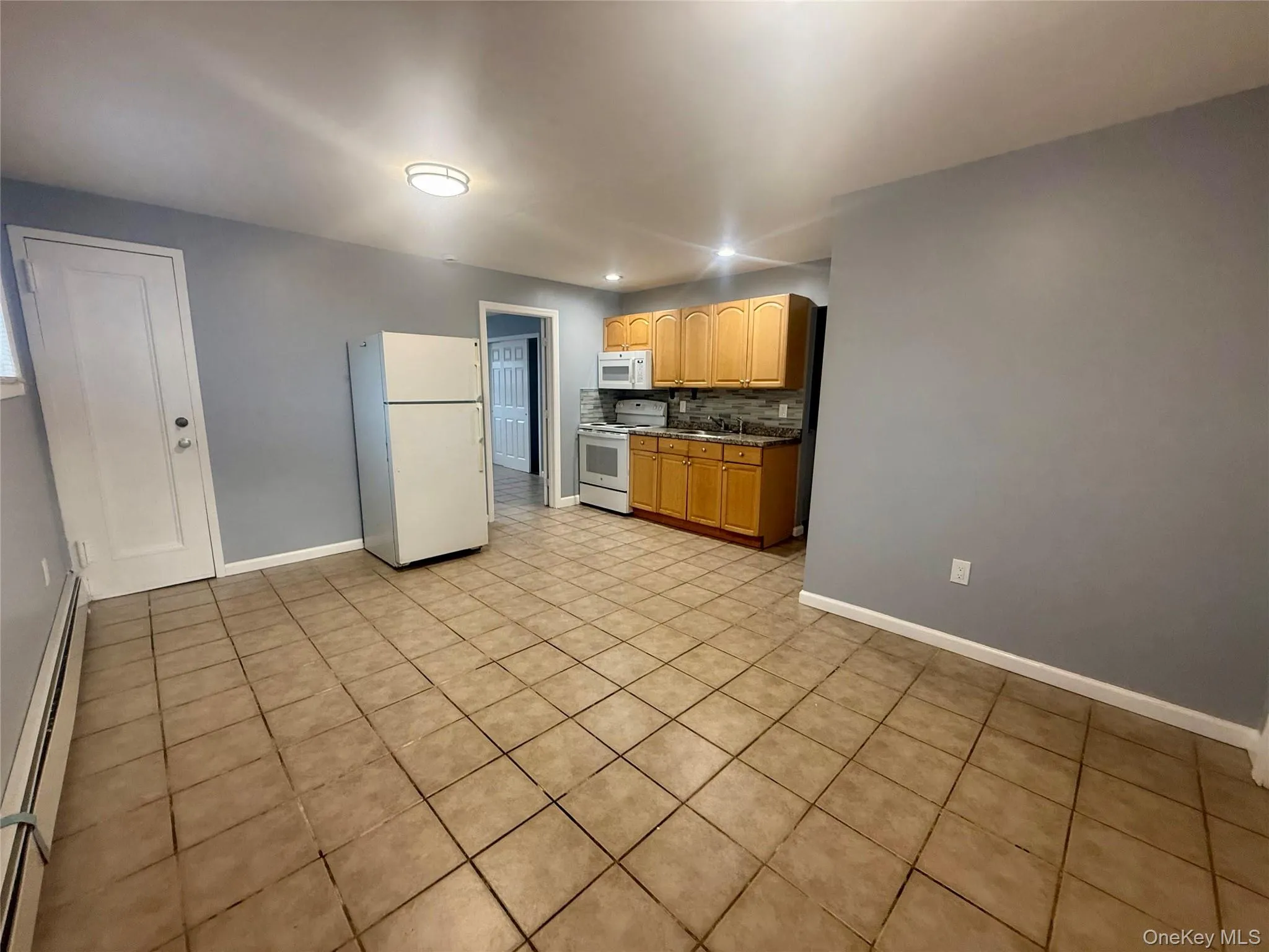 Kitchen featuring tasteful backsplash, white appliances, baseboard heating, light tile patterned floors, and recessed lighting Kitchen featuring tasteful backsplash, white appliances, baseboard heating, light tile patterned floors, and recessed lighting