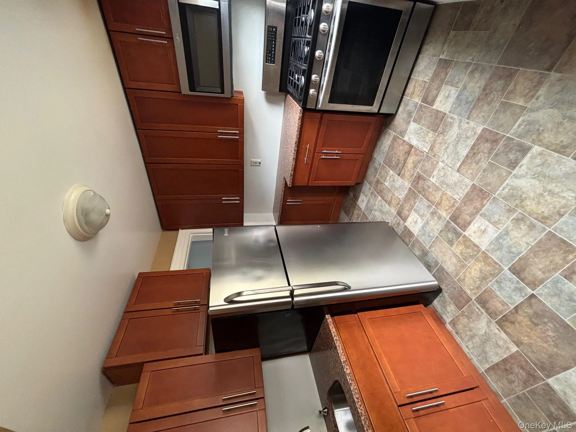 Kitchen with range, stone finish flooring, stainless steel refrigerator, dark stone countertops, and brown cabinetry Kitchen with range, stone finish flooring, stainless steel refrigerator, dark stone countertops, and brown cabinetry