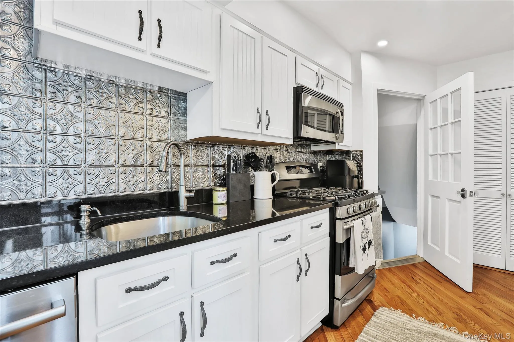 Kitchen featuring stainless steel appliances, backsplash, granite countertops, white cabinets, and hardwood flooring Kitchen featuring stainless steel appliances, backsplash, granite countertops, white cabinets, and hardwood flooring