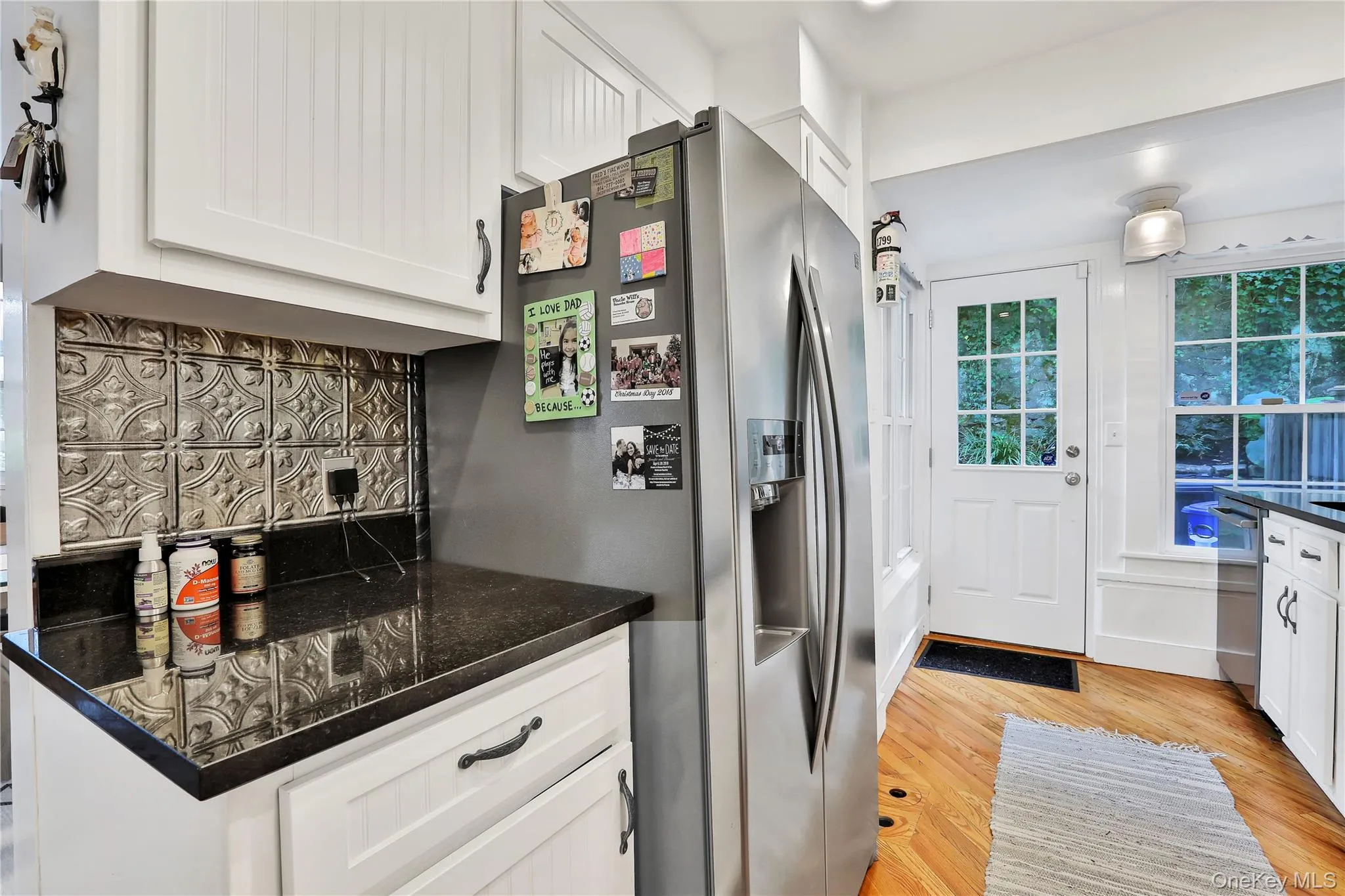 Kitchen featuring backsplash, white cabinets, appliances with stainless steel finishes, hardwood flooring, and granite countertops Kitchen featuring backsplash, white cabinets, appliances with stainless steel finishes, hardwood flooring, and granite countertops
