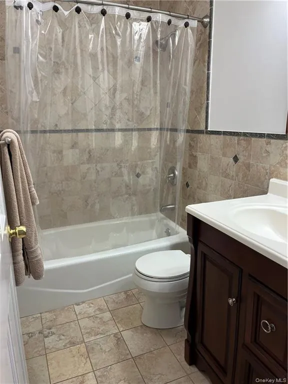 Bathroom with shower / bath combo, vanity, tile walls, and light tile patterned flooring Bathroom with shower / bath combo, vanity, tile walls, and light tile patterned flooring