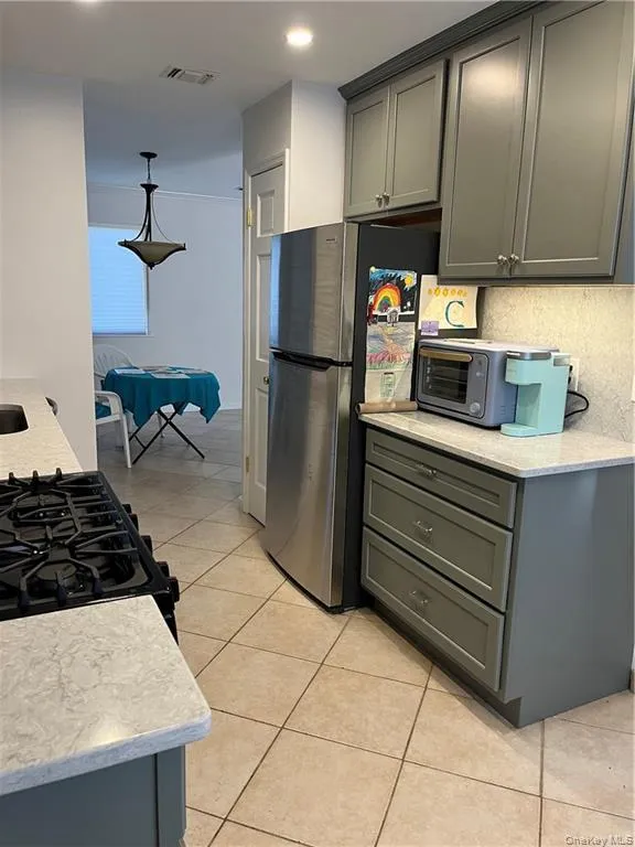 Kitchen with gray cabinetry, gas stove, light tile patterned floors, light stone countertops, and recessed lighting Kitchen with gray cabinetry, gas stove, light tile patterned floors, light stone countertops, and recessed lighting