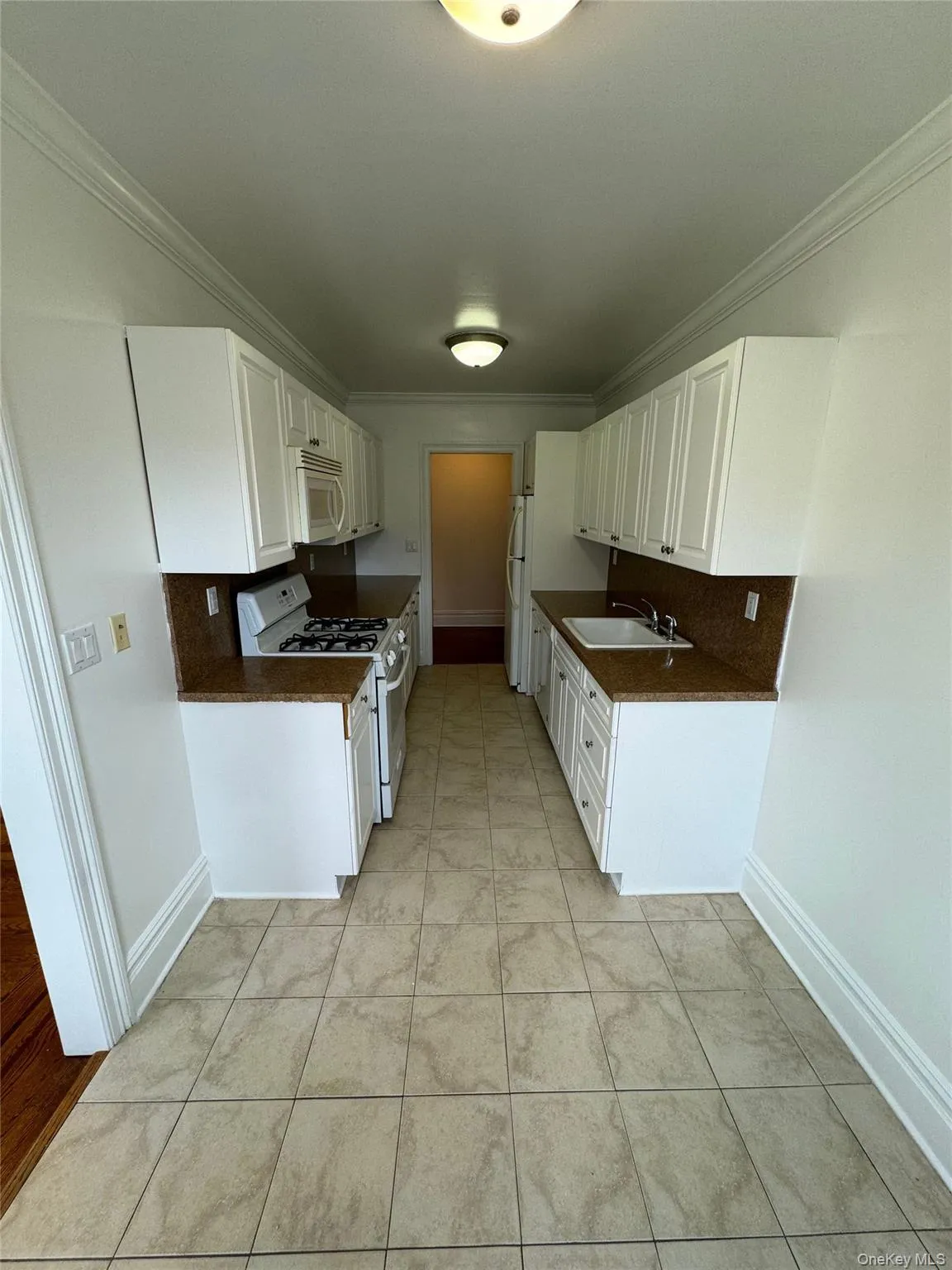 Kitchen with dark countertops, ornamental molding, white appliances, white cabinets, and light tile patterned flooring Kitchen with dark countertops, ornamental molding, white appliances, white cabinets, and light tile patterned flooring
