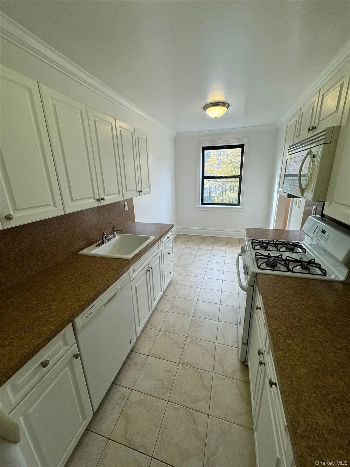 Kitchen with white appliances, crown molding, white cabinetry, and light tile patterned flooring Kitchen with white appliances, crown molding, white cabinetry, and light tile patterned flooring