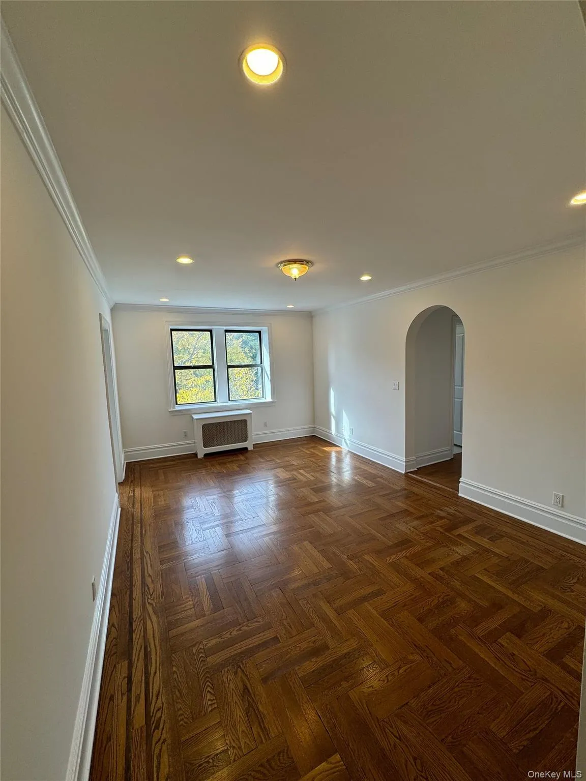 Unfurnished room featuring arched walkways, ornamental molding, recessed lighting, and radiator heating unit Unfurnished room featuring arched walkways, ornamental molding, recessed lighting, and radiator heating unit