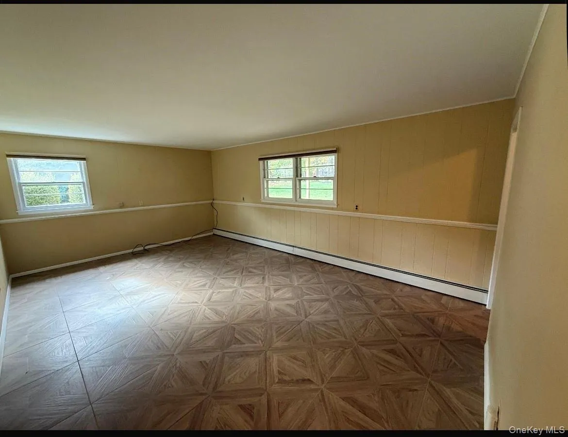 Empty room featuring healthy amount of natural light, baseboard heating, and wood walls Empty room featuring healthy amount of natural light, baseboard heating, and wood walls