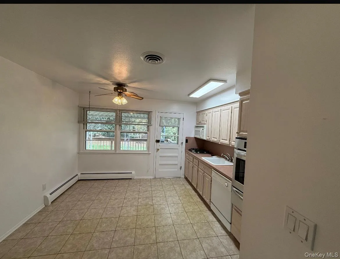 Kitchen featuring a ceiling fan, a baseboard heating unit, white appliances, light countertops, and light tile patterned floors Kitchen featuring a ceiling fan, a baseboard heating unit, white appliances, light countertops, and light tile patterned floors
