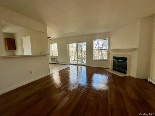 Unfurnished living room with a tile fireplace, dark wood-type flooring, a wall mounted AC, and a baseboard heating unit Unfurnished living room with a tile fireplace, dark wood-type flooring, a wall mounted AC, and a baseboard heating unit