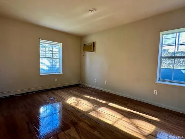 Unfurnished room with dark wood-style flooring, baseboard heating, and an AC wall unit Unfurnished room with dark wood-style flooring, baseboard heating, and an AC wall unit